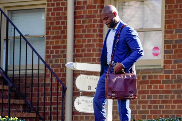 Nathan Wade walks in a cobalt blue suit holding a leather carry bag outside his law offices