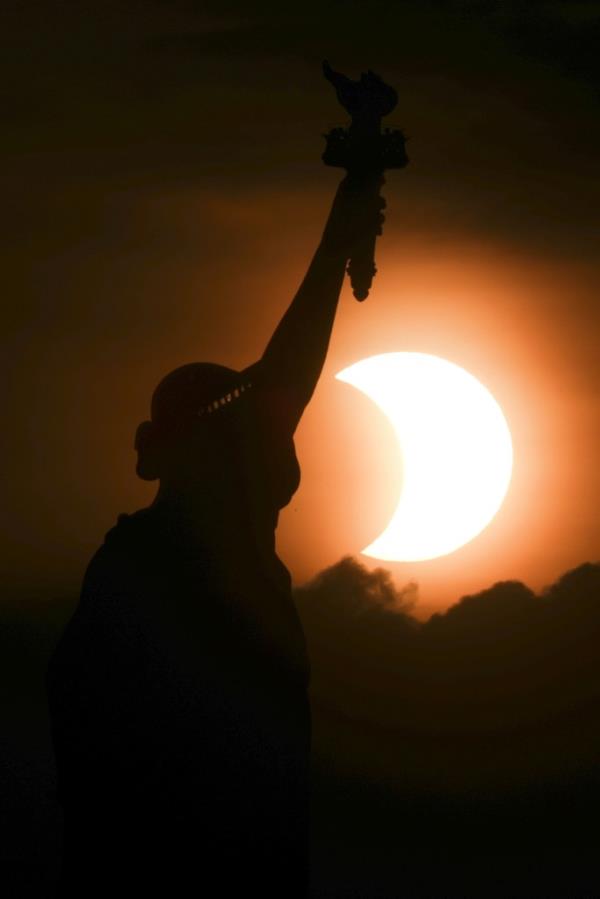 Partially eclipsed sun rising behind the Statue of Liberty in New York City