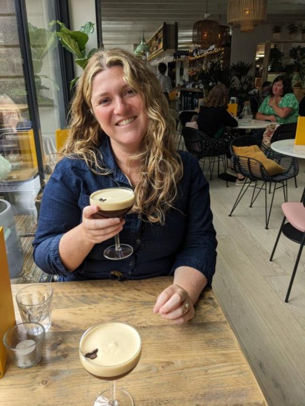 Emmie Harrison-West holding an espresso martini and smiling at the camera, sitting at a table at a bar – another espresso martini opposite her on the table.