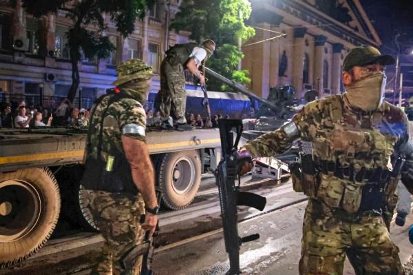 Members of the Wagner Group military company guard an area as other load their tank o<em></em>nto a truck on a street in Rostov-on-Don, Russia, Saturday, June 24, 2023