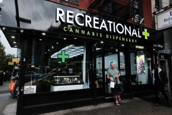 A man standing in front of a legal cannabis dispensary in the East Village, New York City amidst a crackdown on unlicensed smoke shops.