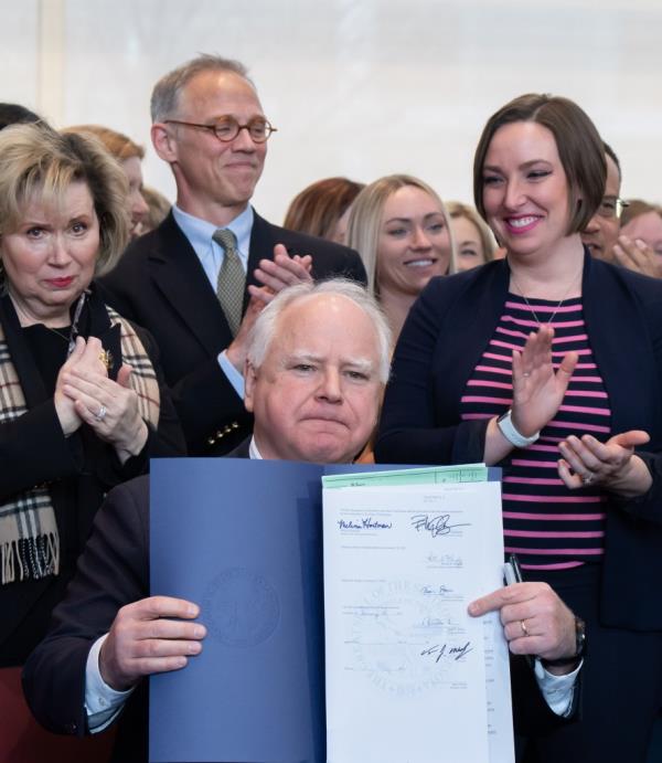 Gov. Tim Walz signs legislation with a cheering crowd behind him 