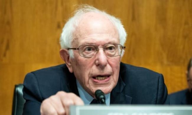 Older white man with white hair and glasses speaks into a microphone.