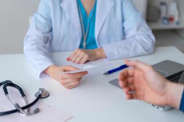 Unrecognizable doctor prescribing pharmacy to patient. Male hand reaching for piece of paper