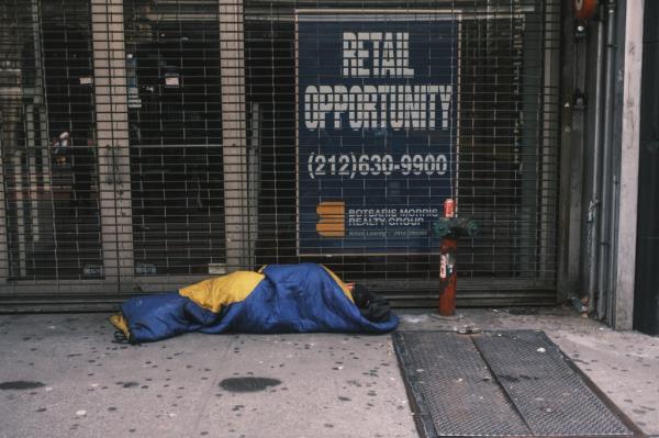 Homeless person sleeping in front of a vacant storefront on 34th street in Manhattan, New York