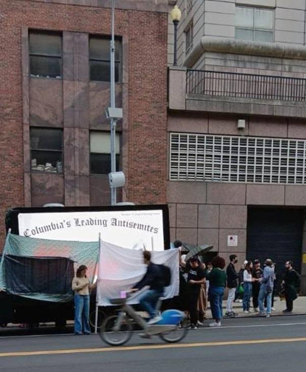 Bystanders gathered in front of the truck with banners and open umbrellas in an effort to shield the names and photos of students the vehicle's digital billboard said were 