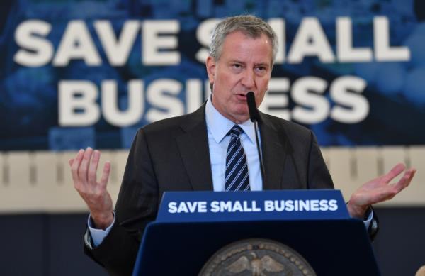 NYC Mayor Bill de Blasio speaking at 'Save Small Business' presser surrounded by small business owners and city officials in a gymnasium