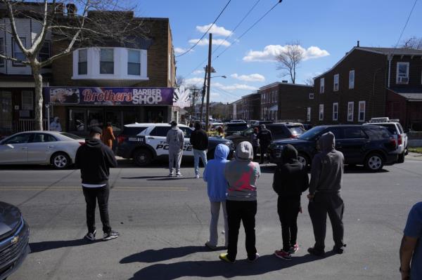 People look on as police surround a home in Trenton, N.J., Saturday, March 16, 2024. 