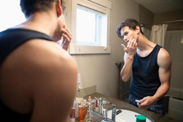 Teenage boy shavin<em></em>g his face in front of a bathroom mirror