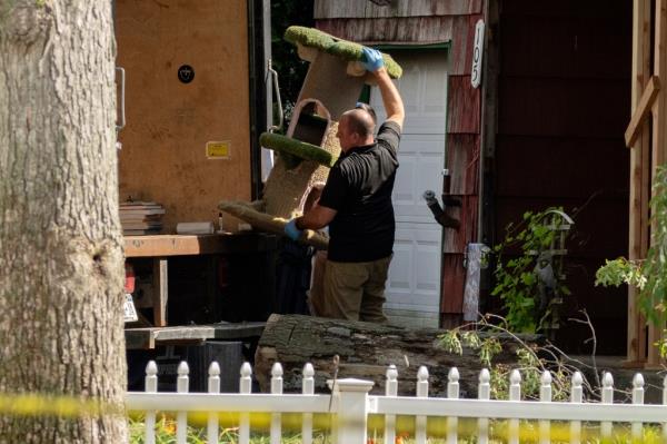 A crime laboratory officer moves a cat scratching post as law enforcement searches the home of Rex Heuermann.