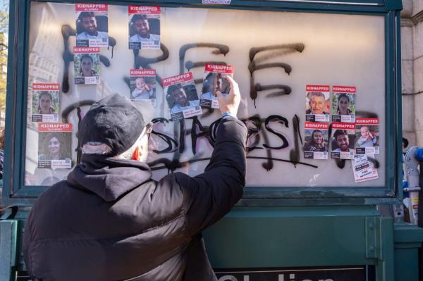 A man putting up hostage posters on a subway sign.