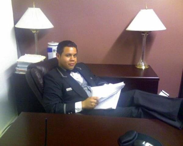 Stephen Bruno in doorman uniform, sitting with legs on desk.