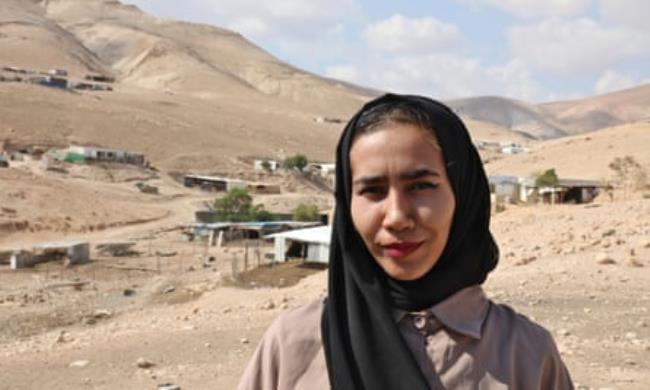 Alia Mlehat, from al-Mu’arrajat – young woman wearing black headscarf and red lipstick, standing against stark landscape